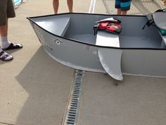 a small boat sitting on top of a cement floor next to people standing near it