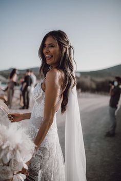 a woman in a wedding dress standing on the side of a road with people around her