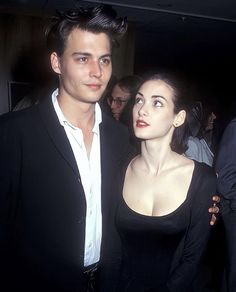 a man standing next to a woman in a black dress at a formal event with other people