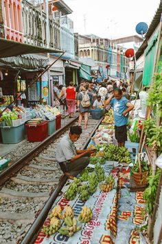 an outdoor market with people shopping and selling fruits and veggies on the tracks