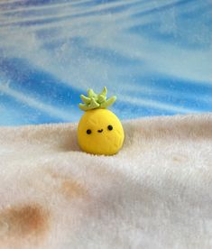 a small yellow toy with a green leaf on it's head sitting in the snow