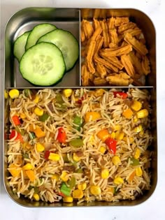 a metal container filled with rice and veggies next to cucumber slices