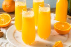 three glasses filled with orange juice on top of a white plate next to sliced oranges