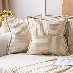 two white pillows sitting on top of a couch next to a vase filled with flowers