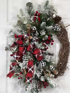 a christmas wreath with red and black plaid bow hanging on the front door, decorated with pine cones