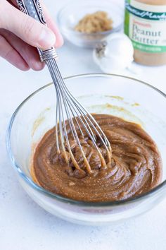 a hand holding a whisk in a bowl with peanut butter and other ingredients