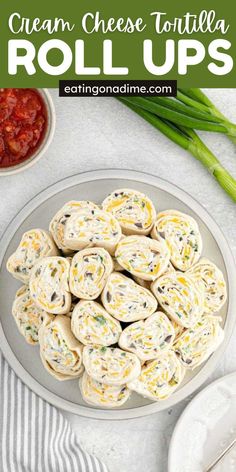 a plate full of cream cheese tortilla rolls with green onions and ketchup on the side