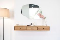 a mirror on the wall above a dresser with drawers and a lamp next to it