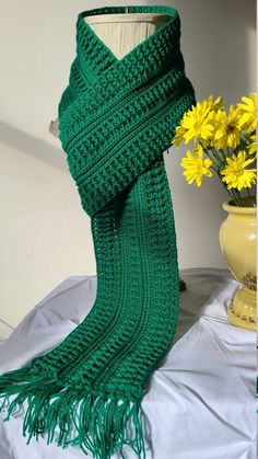 a green scarf sitting on top of a table next to a vase with yellow flowers