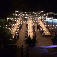 people are sitting at long tables with lights strung over them and in the background, there is an outdoor dining area