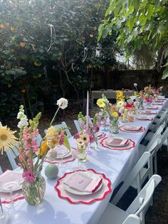 a long table set up with plates and flowers in vases on top of it