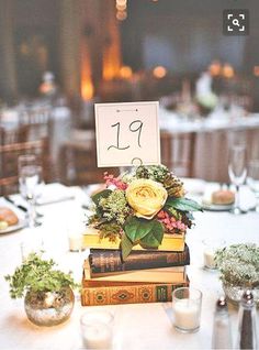 a table topped with lots of books covered in flowers and greenery next to candles