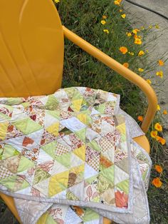 a quilted blanket sitting on top of a yellow chair next to flowers and grass