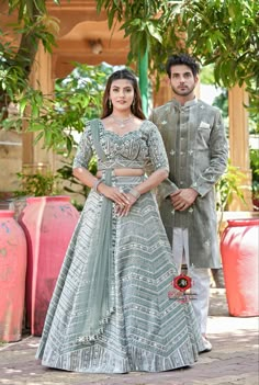 a man and woman standing next to each other in front of a tree with potted plants