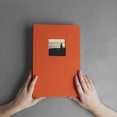 two hands holding an orange book with a photo on it