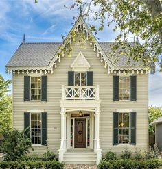 a white house with green shutters and a brown front door on a sunny day