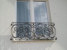 an iron balcony railing on the side of a white building with two windows and sky in the background