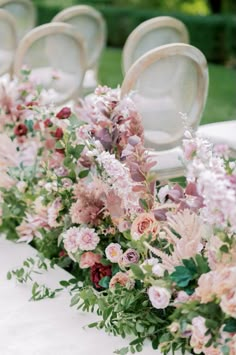 rows of white chairs with pink flowers and greenery lined up along the back of them