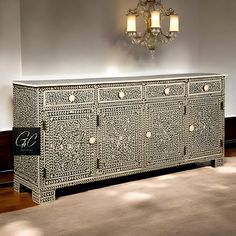 an ornately decorated sideboard with two lamps on the wall and a chandelier above it