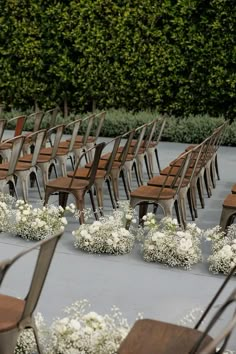 rows of wooden chairs with white flowers on the ground in front of trees and bushes