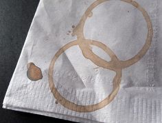 a napkin with an olympic symbol drawn on it and brown ink splatters all over the paper