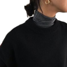 a woman wearing a black turtle neck sweater and large gold hoop earrings, looking off to the side