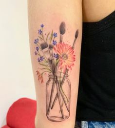 a woman's arm with flowers and brushes in a mason jar tattoo on it