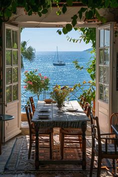 an open door leading to a table with flowers on it and a sailboat in the distance