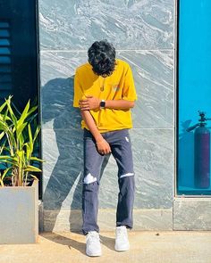 a man leaning against a wall with his hand on his chest and wearing a yellow shirt