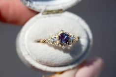 a person holding an open ring with a purple and white stone in it's center