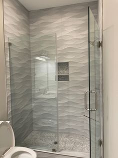 a white toilet sitting next to a shower in a bathroom under a window with wavy glass on the walls