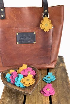 a brown leather bag sitting on top of a wooden table next to small colorful flowers