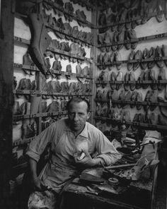 a man sitting at a table in front of many pairs of shoes on display behind him