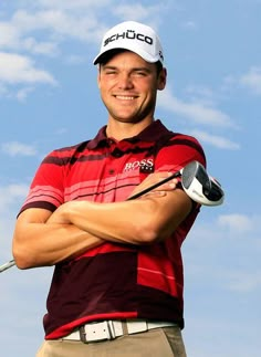 a man in a red and black shirt holding a golf club with his arms crossed