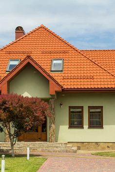 a house with a red tiled roof and two trees in the front yard, on a sunny day