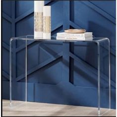 a clear console table with books and vases on it in front of a blue wall