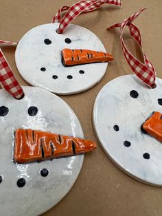 three ceramic snowmen with carrots on their faces hanging from red and white ribbons