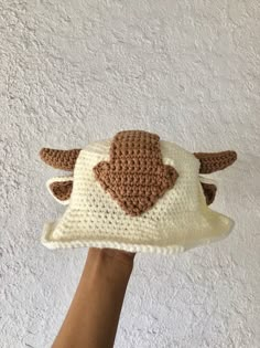 a hand holding up a crocheted hat with an animal on it's side