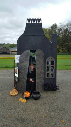 a woman standing in front of a fake house with brooms and pots on the ground