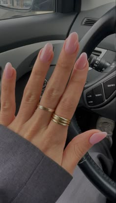 Young woman hand with a fresh manicure wearing some light pink nail polish on almond nails, with two golden stackable rings in a black car. Light Pink With Design Nails, Pale Pink Nails Almond Shape, Gel Nails Inspo Almond, Simple Clear Pink Nails, Pink Clear Almond Nails, Light Pink Gel X Nails, Light Clear Pink Nails, Pink Clear Nails Acrylic, Clear Light Pink Nails