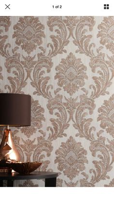 a table with a lamp on it next to a wallpapered background that looks like damask