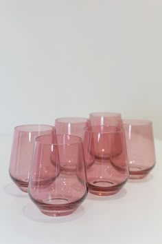 five pink wine glasses lined up on a white counter top with one empty glass in the middle