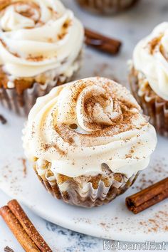 cinnamon cupcakes with white frosting and cinnamon sticks around them on a plate