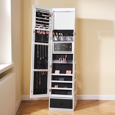 a white mirrored jewelry cabinet in a room with hard wood flooring and beige walls