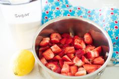 strawberries in a bowl next to a glass of milk and a lemon on a table