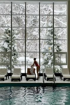 a man sitting on the edge of a swimming pool in front of a large window