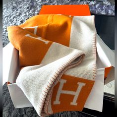 an orange and white blanket sitting in a box on top of a carpeted floor