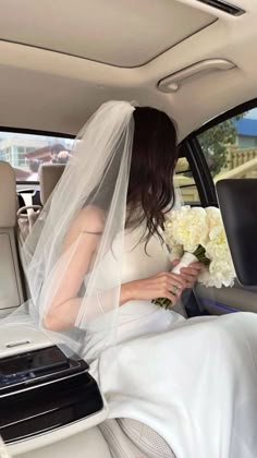 a bride sitting in the back seat of a car with her veil over her head