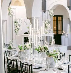 the table is set with white flowers and greenery in tall glass vases on each side