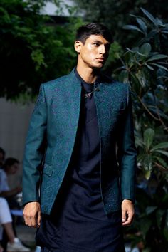 a man is walking down the runway wearing a blue suit and black shirt with a green blazer